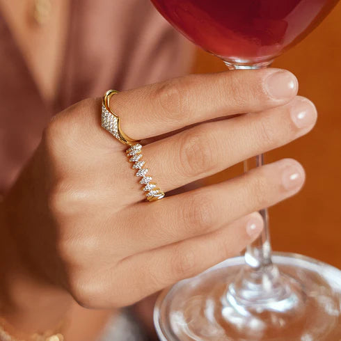 Hand wearing a diamond look ring holding a glass of red wine against an orange background